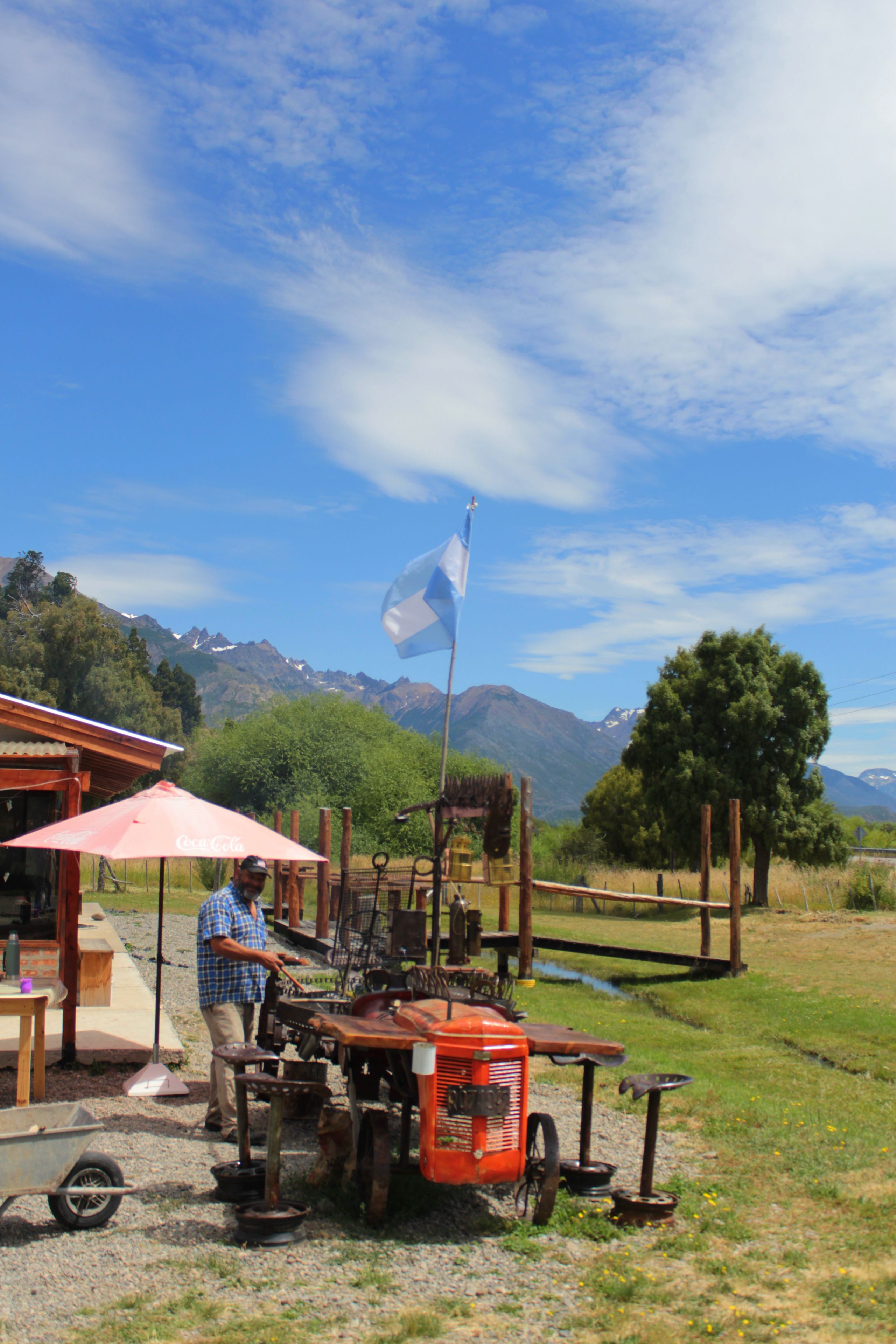 A man operating a vintage orange tractor in a rural setting with mountains in the background.