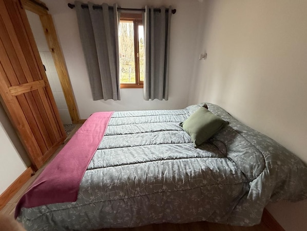 A bedroom with a bed, a window with curtains, and a wooden door. - Don Edmundo Trevelin (Trevelin)