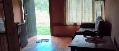 A room with a wooden ceiling, a table with chairs, a window with curtains, and a door leading outside.