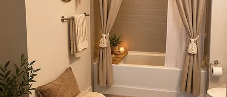 A bathroom with a bathtub, two towels, a mirror, and a plant.