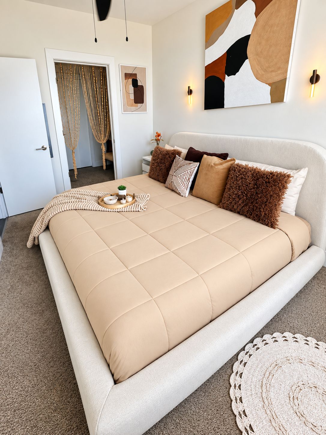 Une chambre à coucher avec un grand lit, une table de chevet, une décoration murale en macramé et un luminaire fixé au mur.