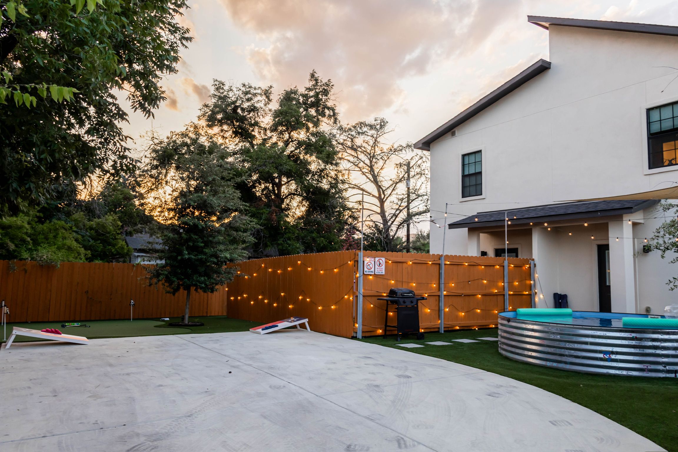 A modern house with a fenced backyard, a swimming pool, and string lights.