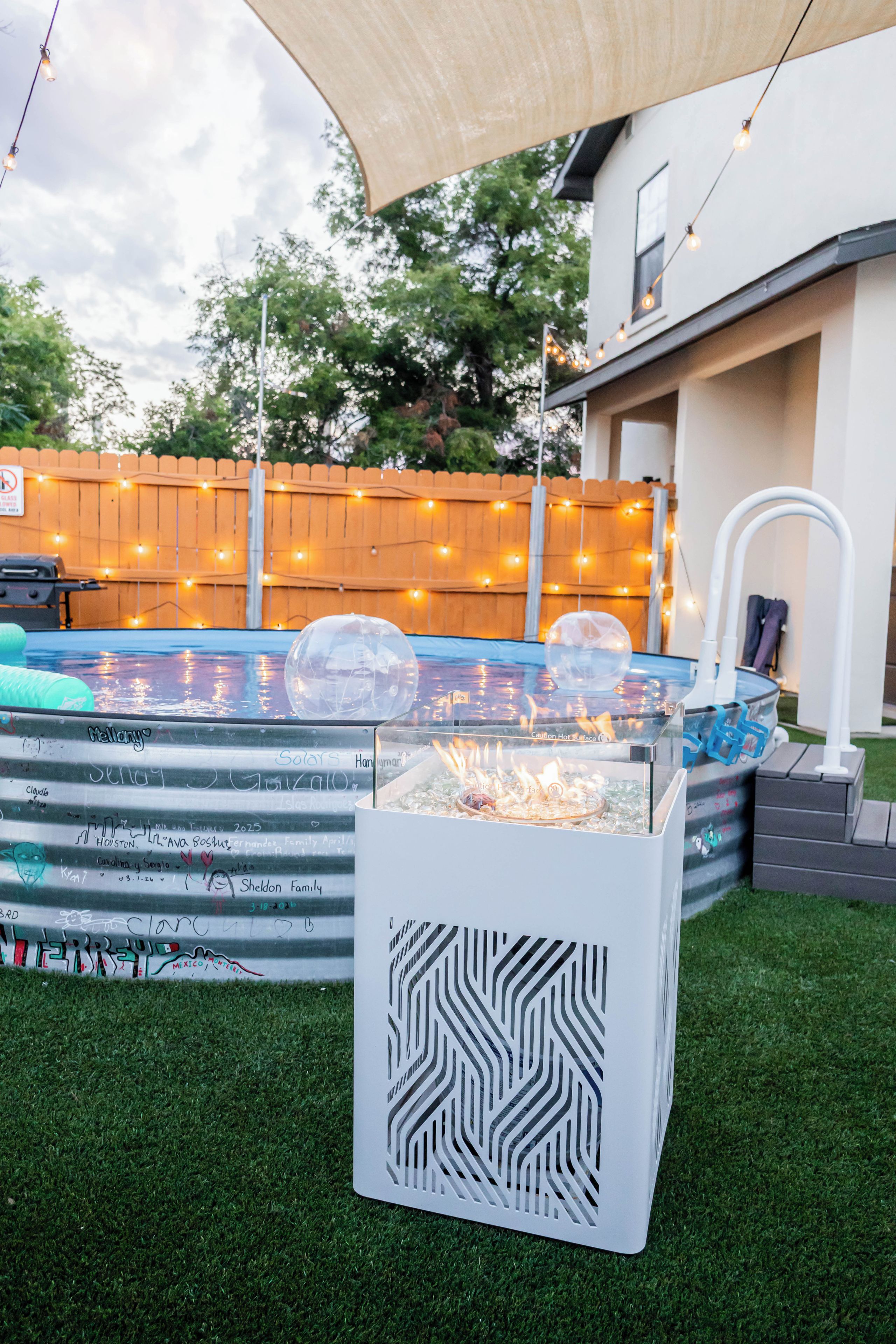 Ein Garten mit Swimmingpool, aufblasbaren Bällen, einer Feuerstelle und einem überdachten Grillbereich.