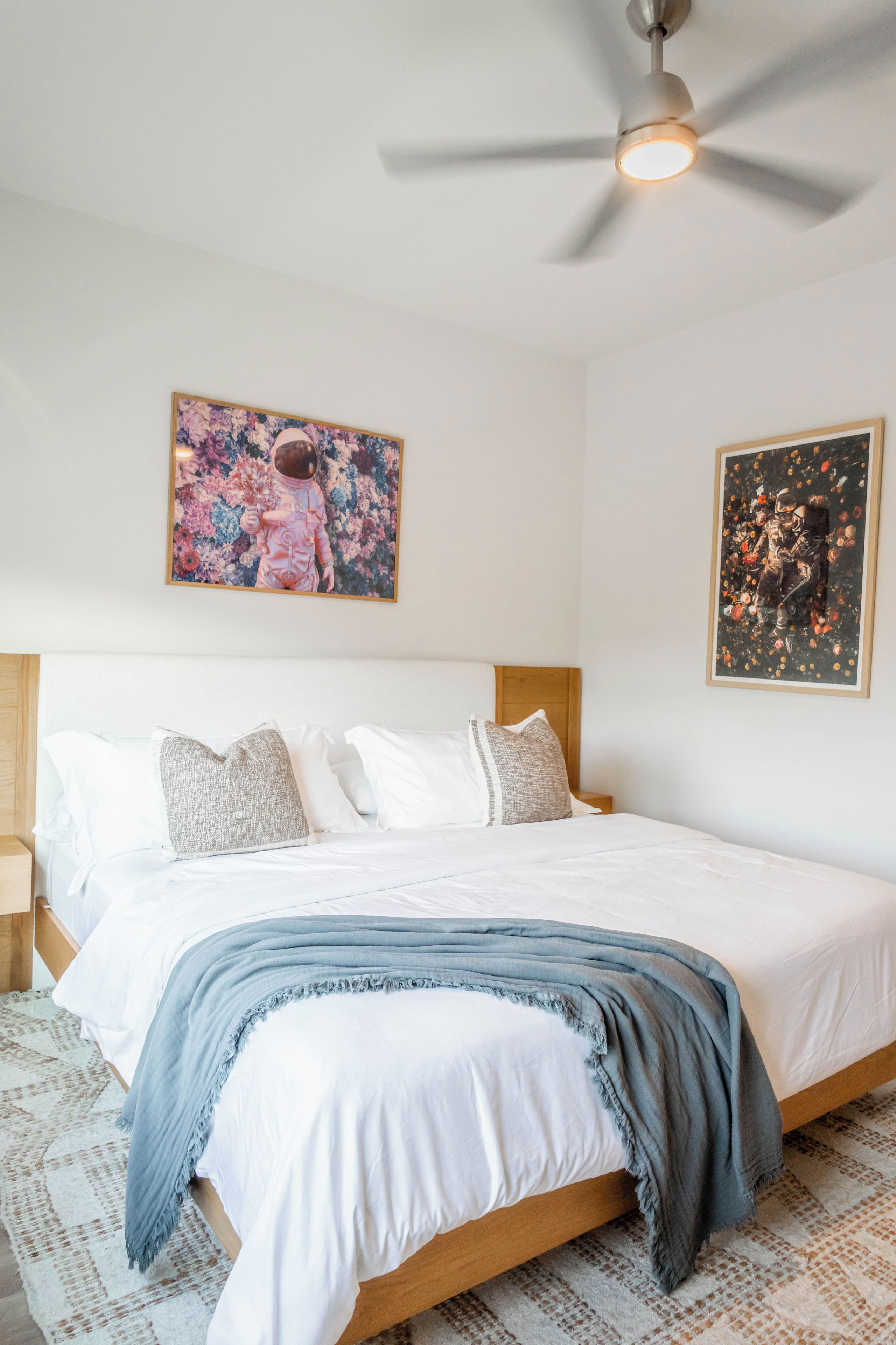 Ein Schlafzimmer mit einem Bett, Kissen, einem Deckenventilator und zwei gerahmten Kunstwerken an der Wand.