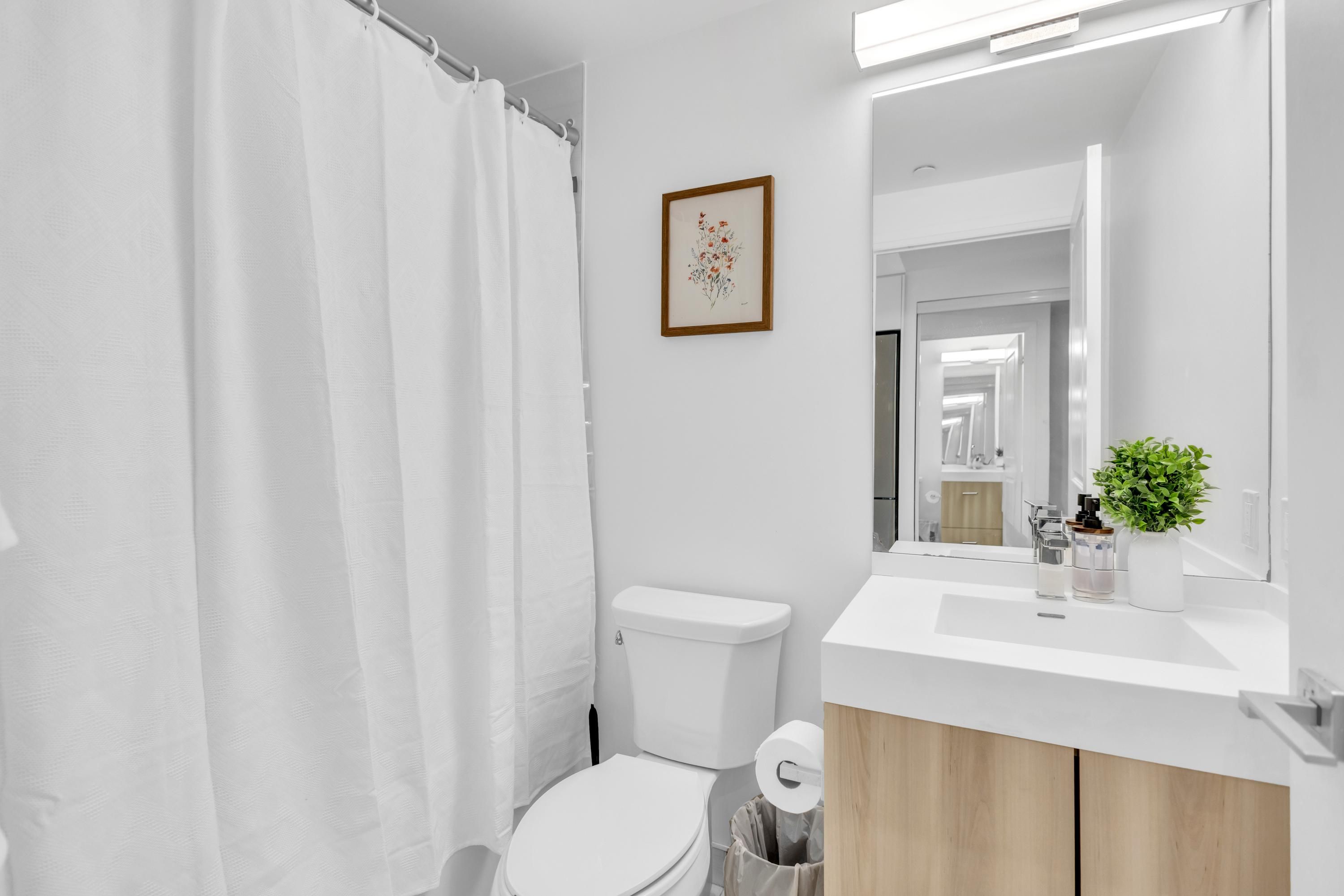 A modern bathroom with a toilet, a shower curtain, a sink with a mirror, and a framed picture on the wall.