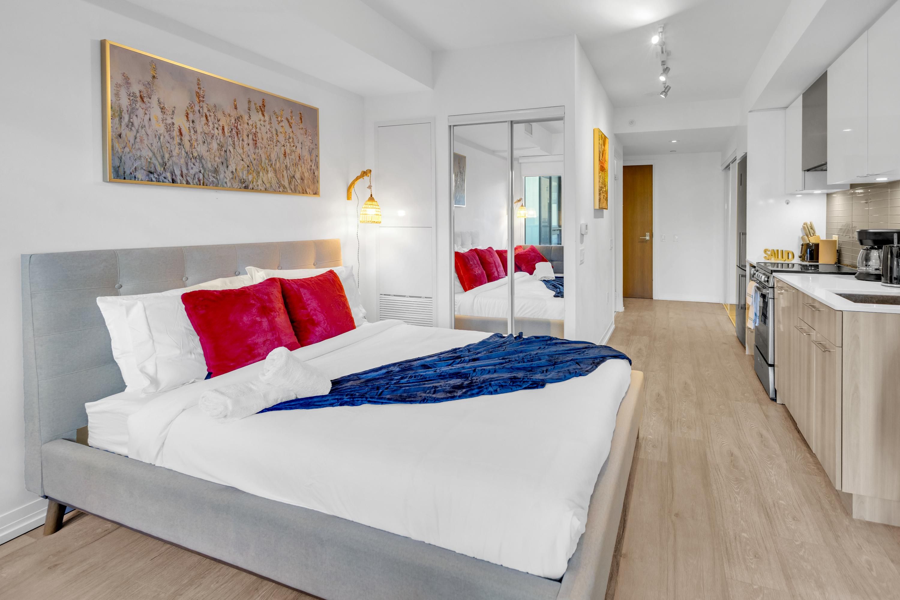 A modern hotel room with a large bed, a separate kitchenette, and a view into the living area.