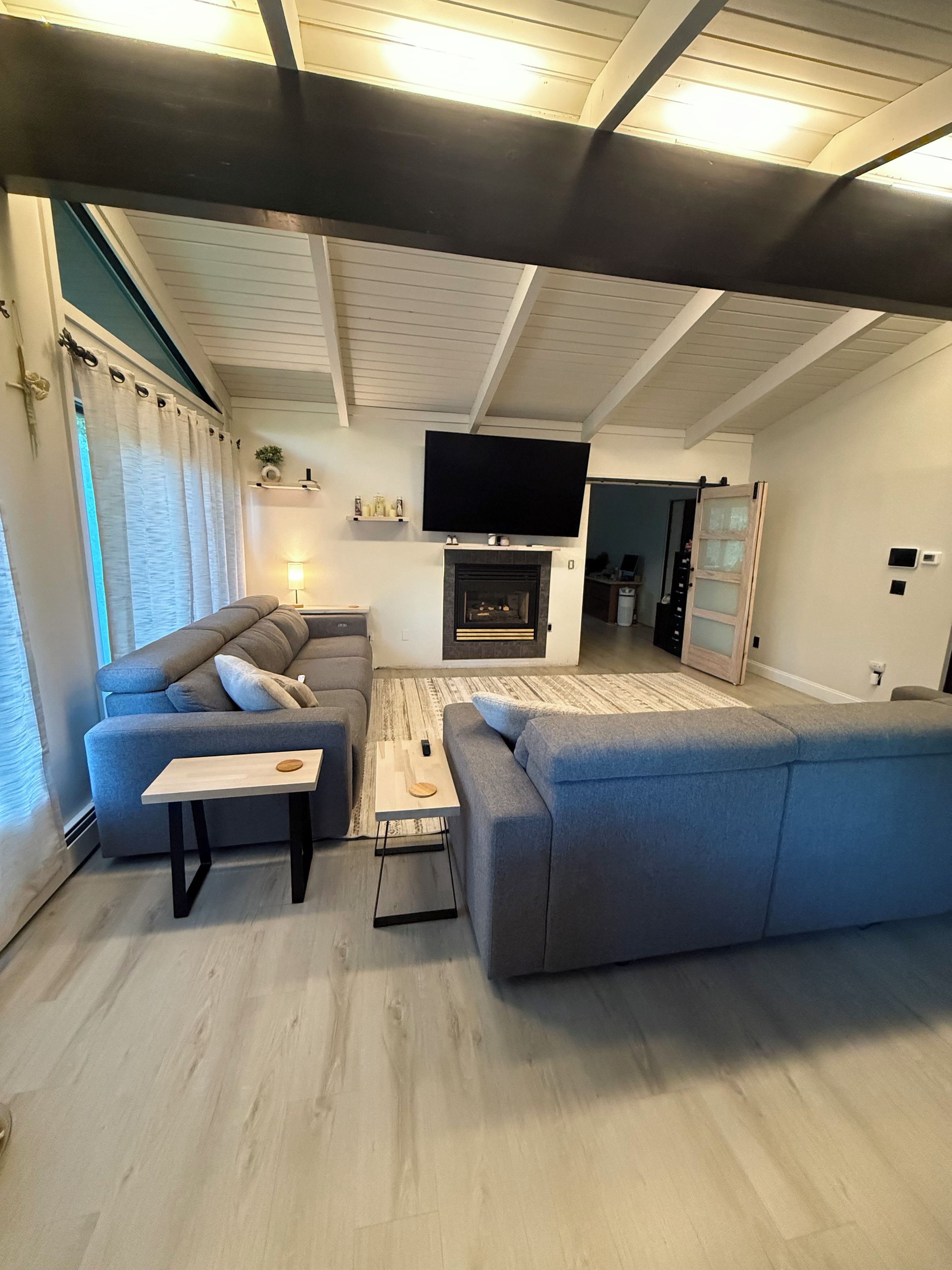 Ein modernes Wohnzimmer mit einer großen, grauen Eckcouch, einem Flachbildfernseher über einem Kamin und einem Couchtisch aus Holz.