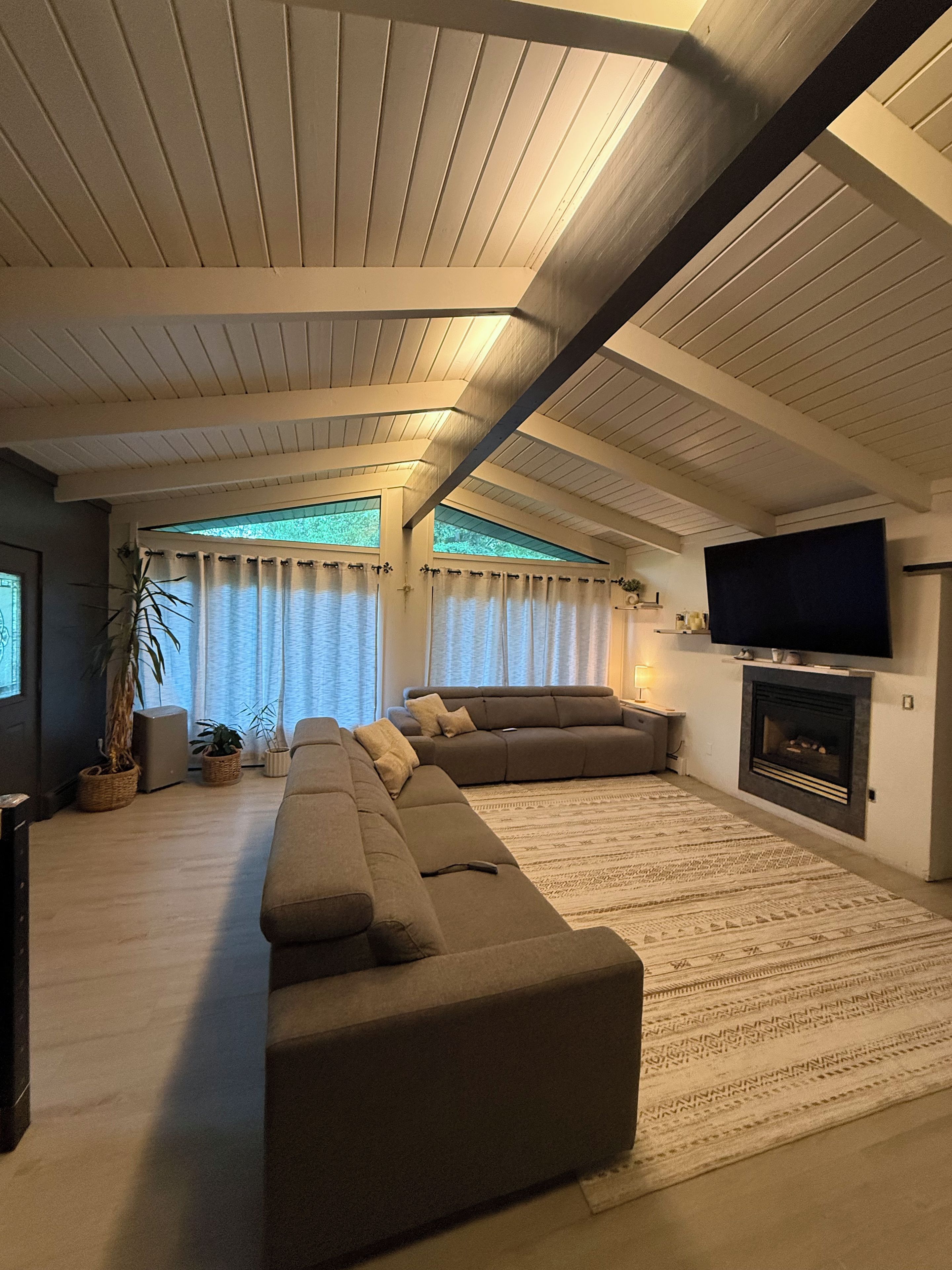 A living room with a sectional sofa, a flat-screen TV mounted on the wall, and a fireplace.
