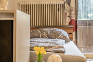 Une chambre à coucher avec un lit, un radiateur, une fenêtre avec des rideaux et une vue sur le ciel.