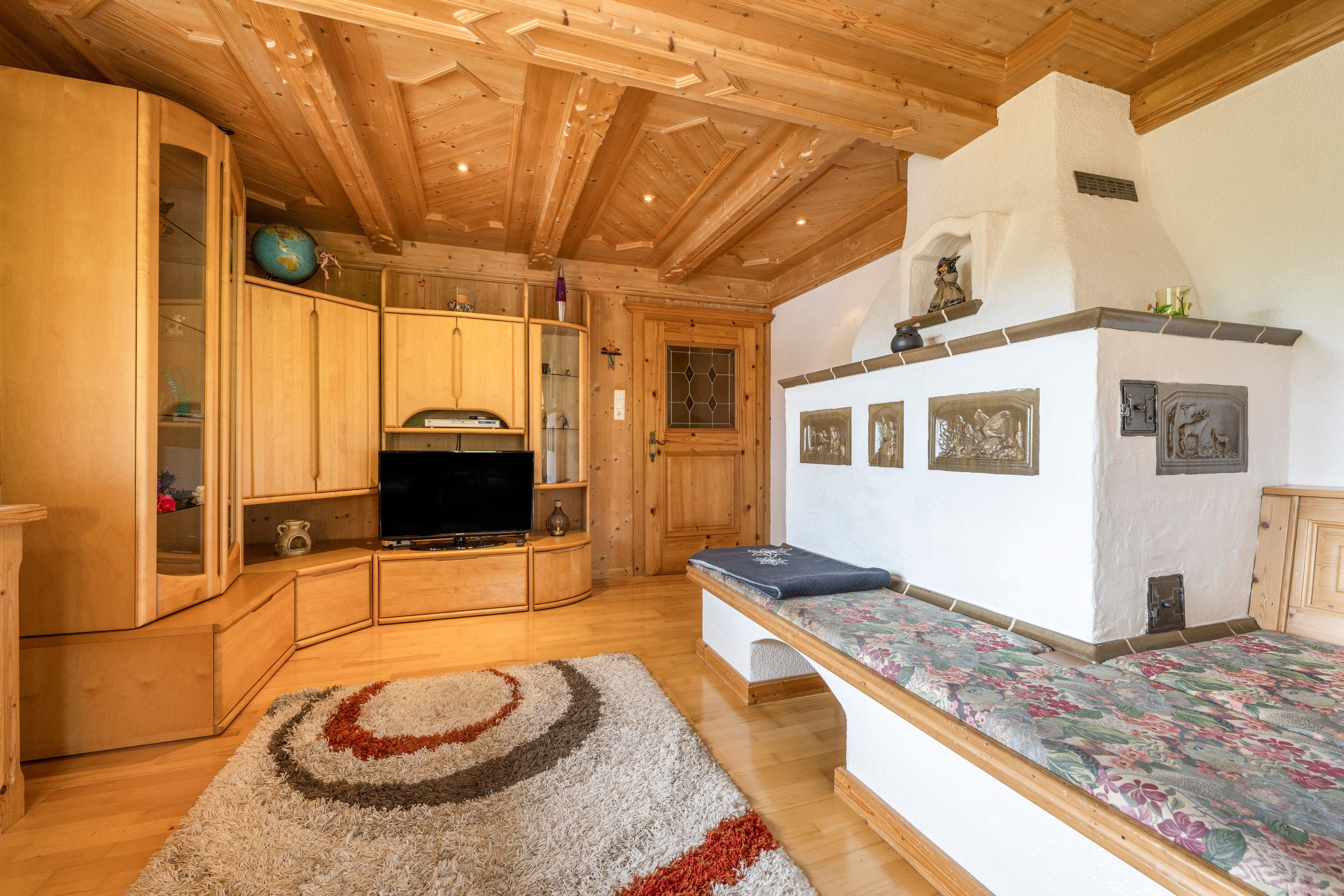 A wooden interior with a television, cabinets, and a patterned rug.