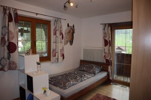 Een slaapkamer met een bed, een radiator, een raam met gordijnen en een aan de muur bevestigde decoratie van een paardenkop.