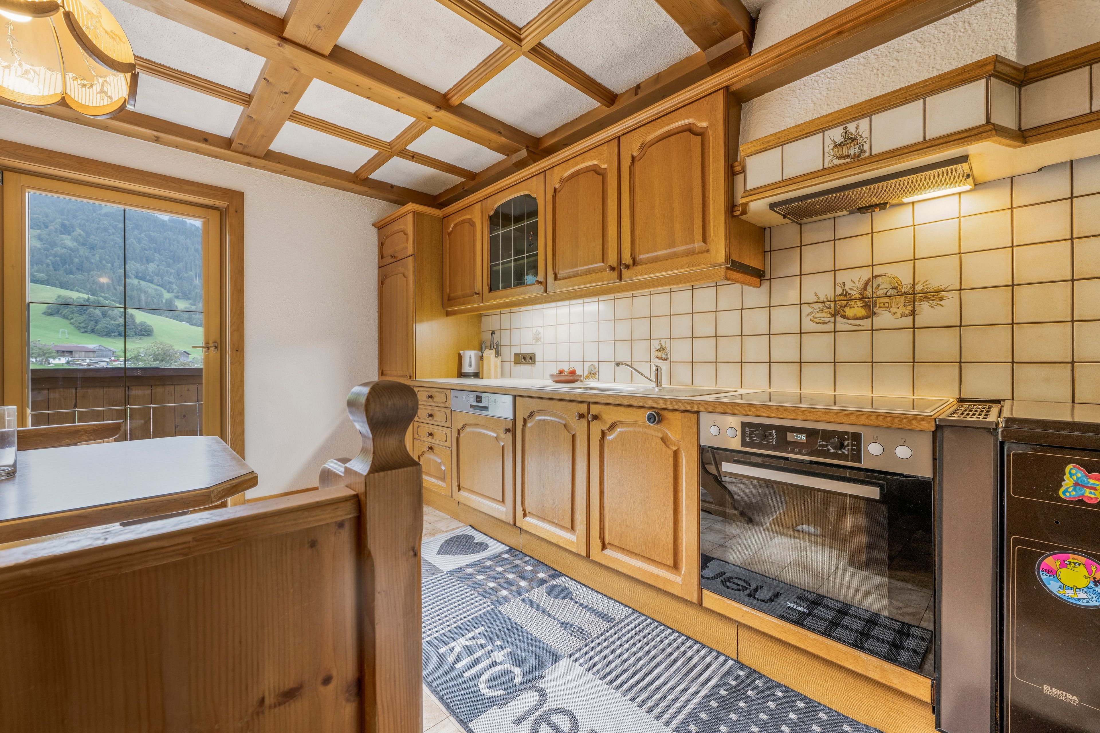 Een keuken met houten kastjes, een inbouwoven en een raam met uitzicht op een schilderachtig landschap.