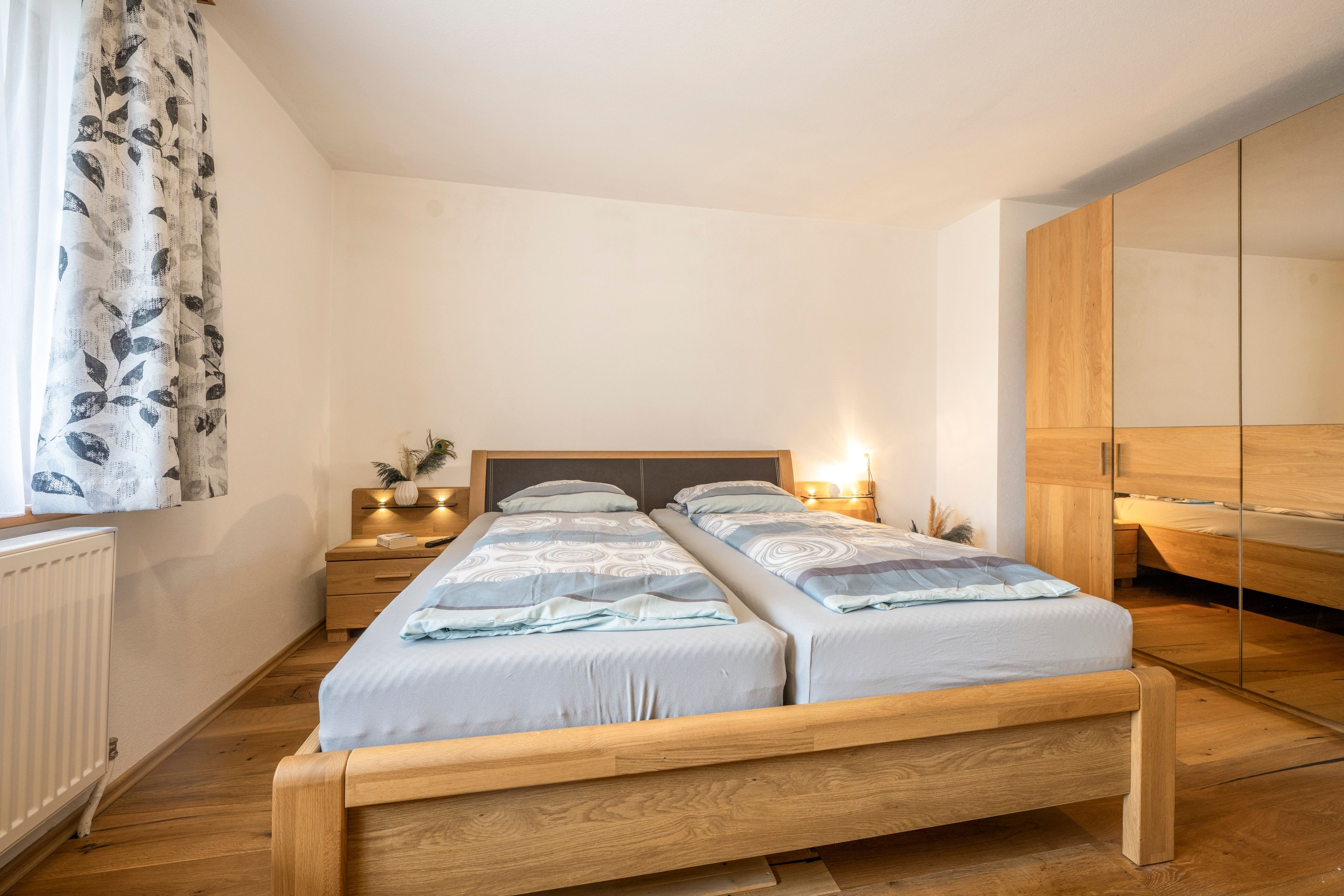 Een tweepersoonsbed met houten frame, een nachtkastje met lamp en een spiegel aan de muur.