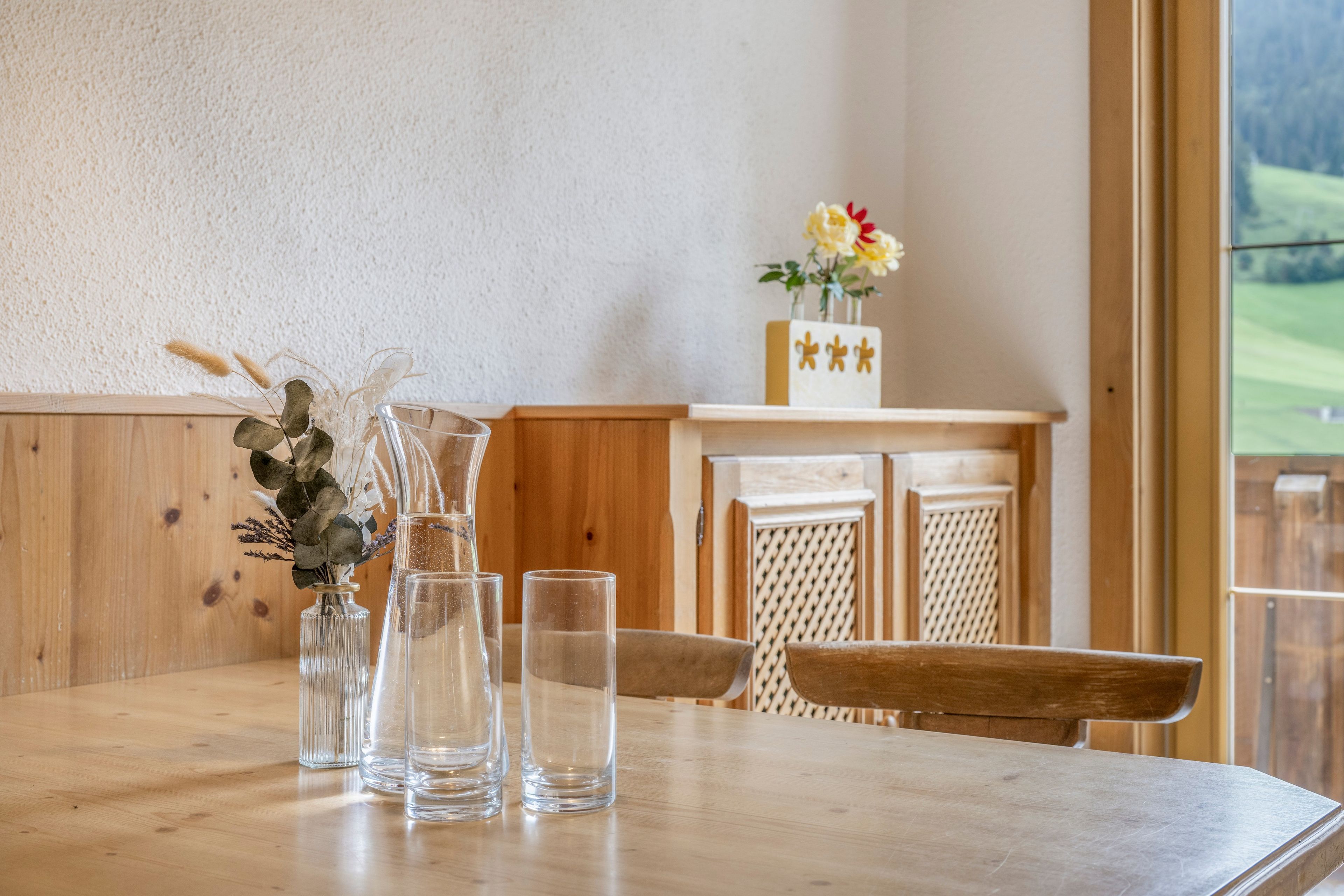 Mesa de madeira com garrafas de vidro transparente e um vaso com plantas secas.