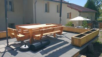 An outdoor patio with a wooden table and benches, surrounded by a low wooden fence and a raised planter box.