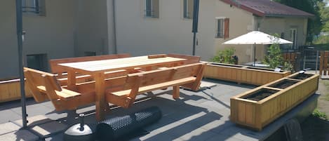 An outdoor patio with a wooden table and benches, surrounded by a low wooden fence and a raised planter box.