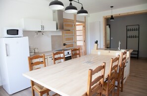 A modern kitchen with a central island, wooden chairs, a white refrigerator, and pendant lighting. - “Gîte La Sainte Juliette” Apartment with Mountain View, Shared Terrace, and Wi-Fi (La Rixouse)