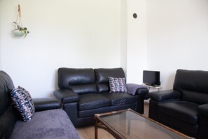 A living room with a black leather sofa, a glass coffee table, and a television on a stand. - “Gîte La Sainte Juliette” Apartment with Mountain View, Shared Terrace, and Wi-Fi (La Rixouse)