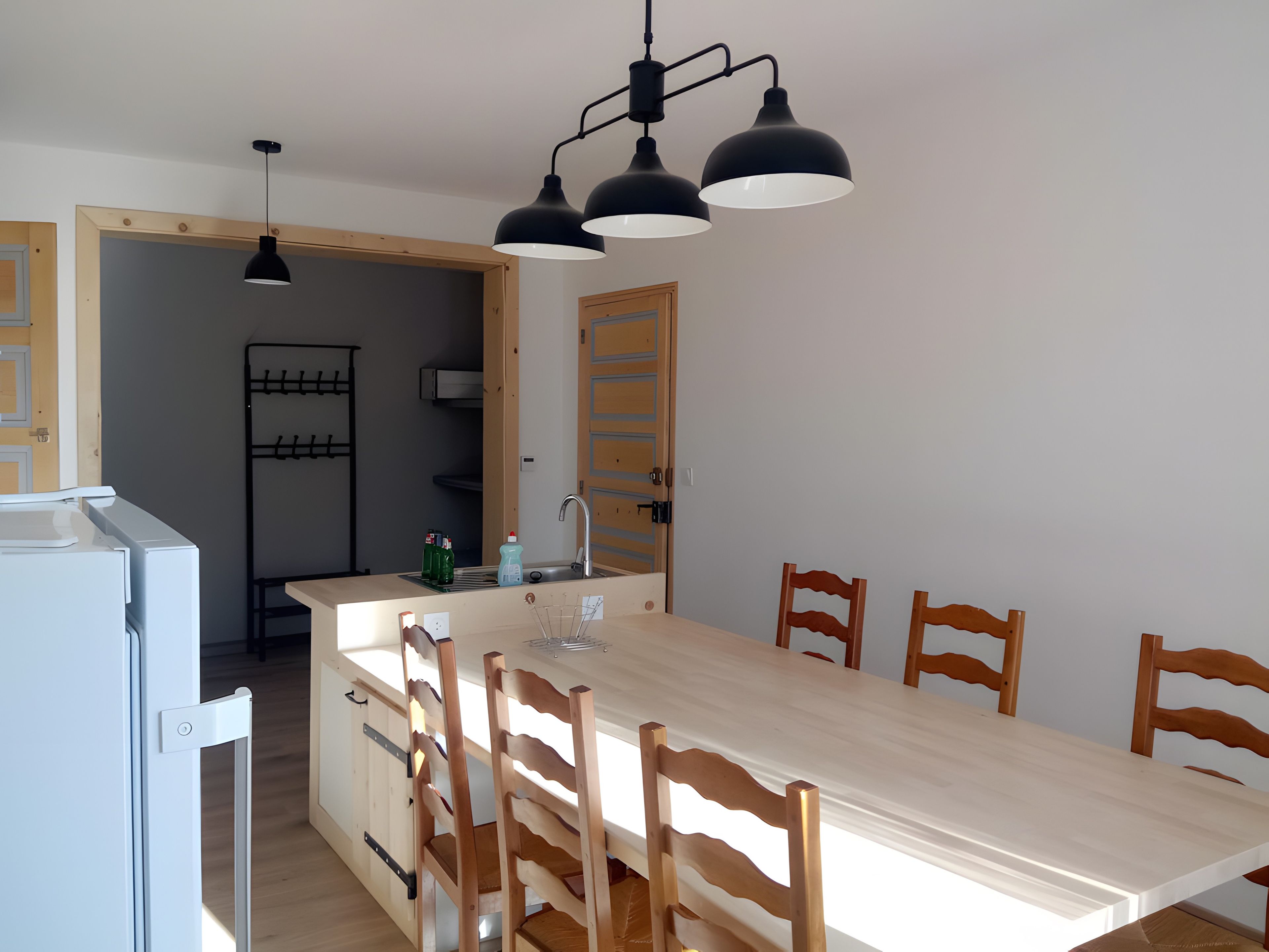 A kitchen with a wooden table and chairs, a sink, and a hanging light fixture.