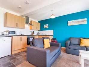 A compact living space with a kitchenette, two sofas, and a blue accent wall. - Private Beach-Front Apartment on the English Riviera with free, private parking (Paignton)