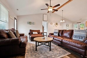 A living room with leather sofas, a coffee table, a ceiling fan, and a patterned rug. - Creekside on 11 Acres | Hot Tub | Wood Fire Pit (Sevierville)