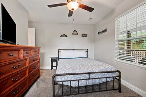 Ein Schlafzimmer mit Bett, Schminktisch, Deckenventilator und Fenster mit Jalousien.