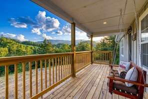 Une terrasse en bois avec un fauteuil suspendu et des coussins, offrant une vue sur un paysage montagneux.