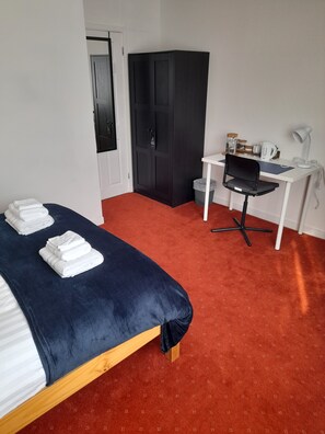 Una habitación con cama, escritorio, silla, armario y cubo de basura.