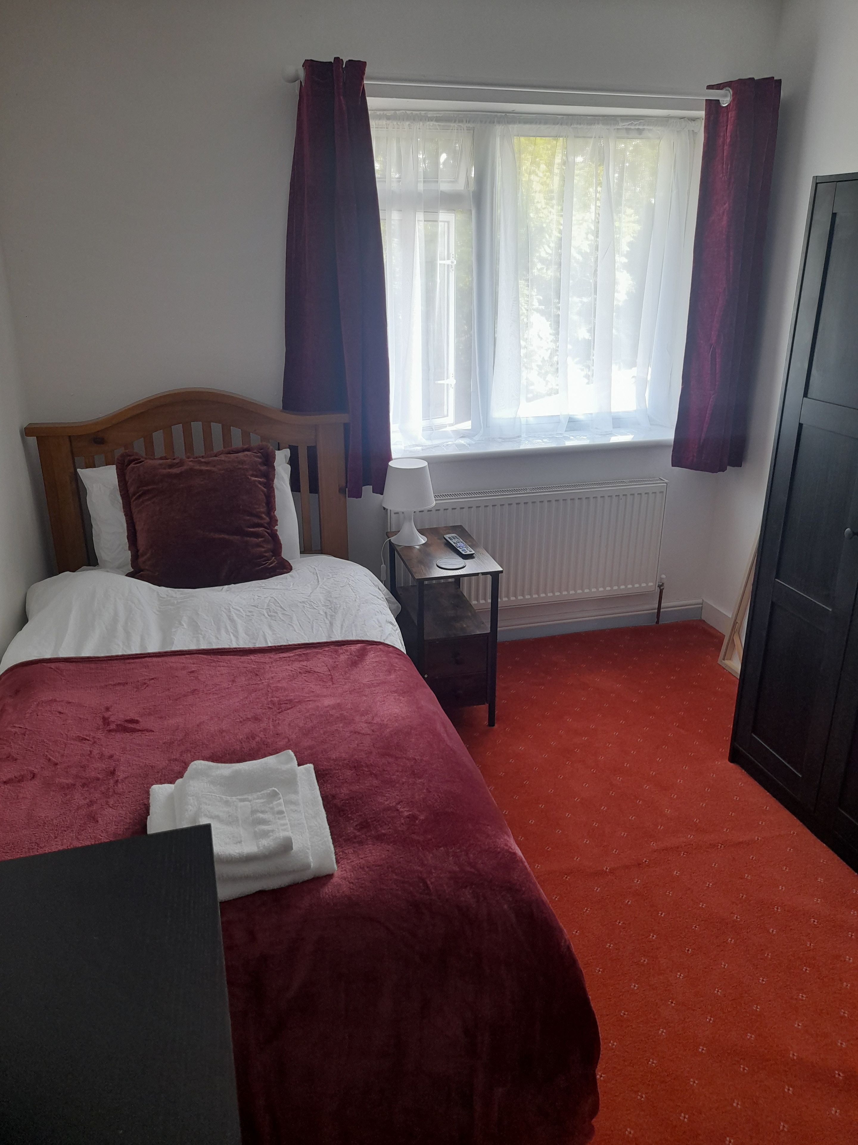 Un dormitorio con cama, una mesita de noche con lámpara, un radiador y una ventana con cortinas.