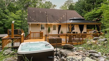 A cabin with a hot tub, deck, and outdoor seating area surrounded by trees.
