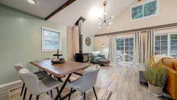 A dining area with a wooden table and chairs, a fireplace, and a view of the outdoors through large windows.