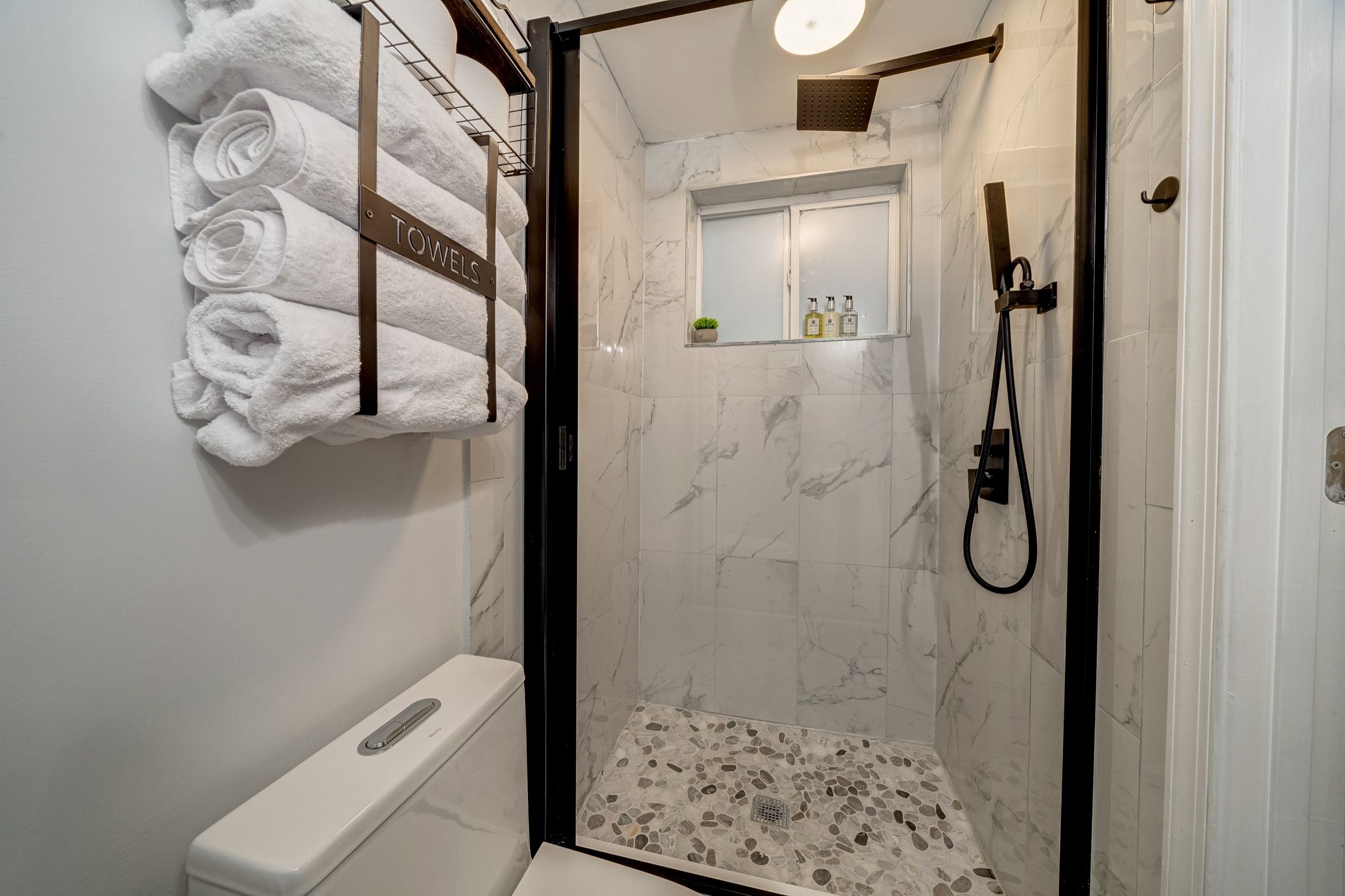 A shower area with a glass door, a toilet, and a towel rack with folded towels.