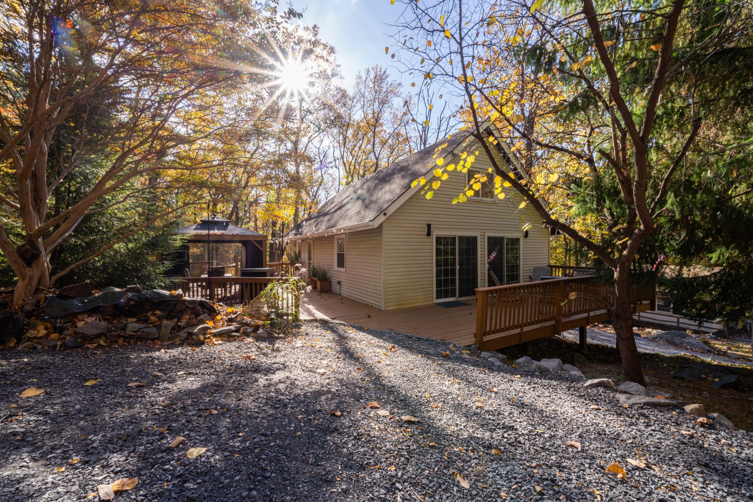 A cabin with a gravel driveway, wooden deck, and a covered outdoor seating area.