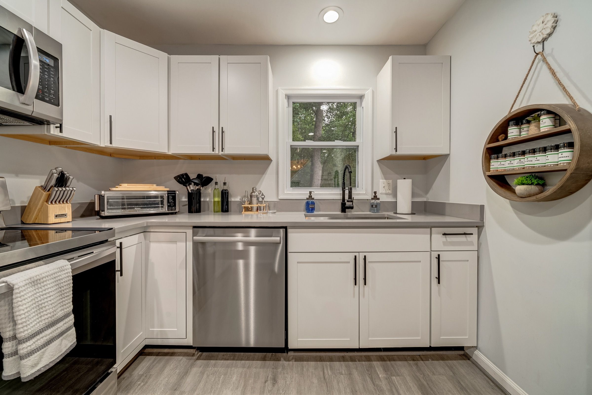 A modern kitchen with white cabinetry, a built-in dishwasher, a microwave, and a window above the sink.