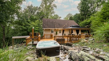 A cabin with a hot tub, wooden deck, and a stone pathway leading to the entrance.