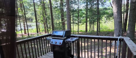 A wooden deck with a grill and a view of a forest.