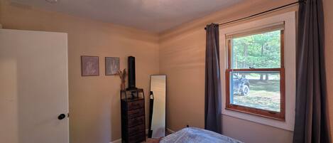 A bedroom with a bed, a dresser, a mirror, and a window with curtains.