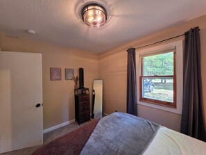 Ein Schlafzimmer mit Bett, Kommode, Spiegel und einem fenster mit Vorhängen.