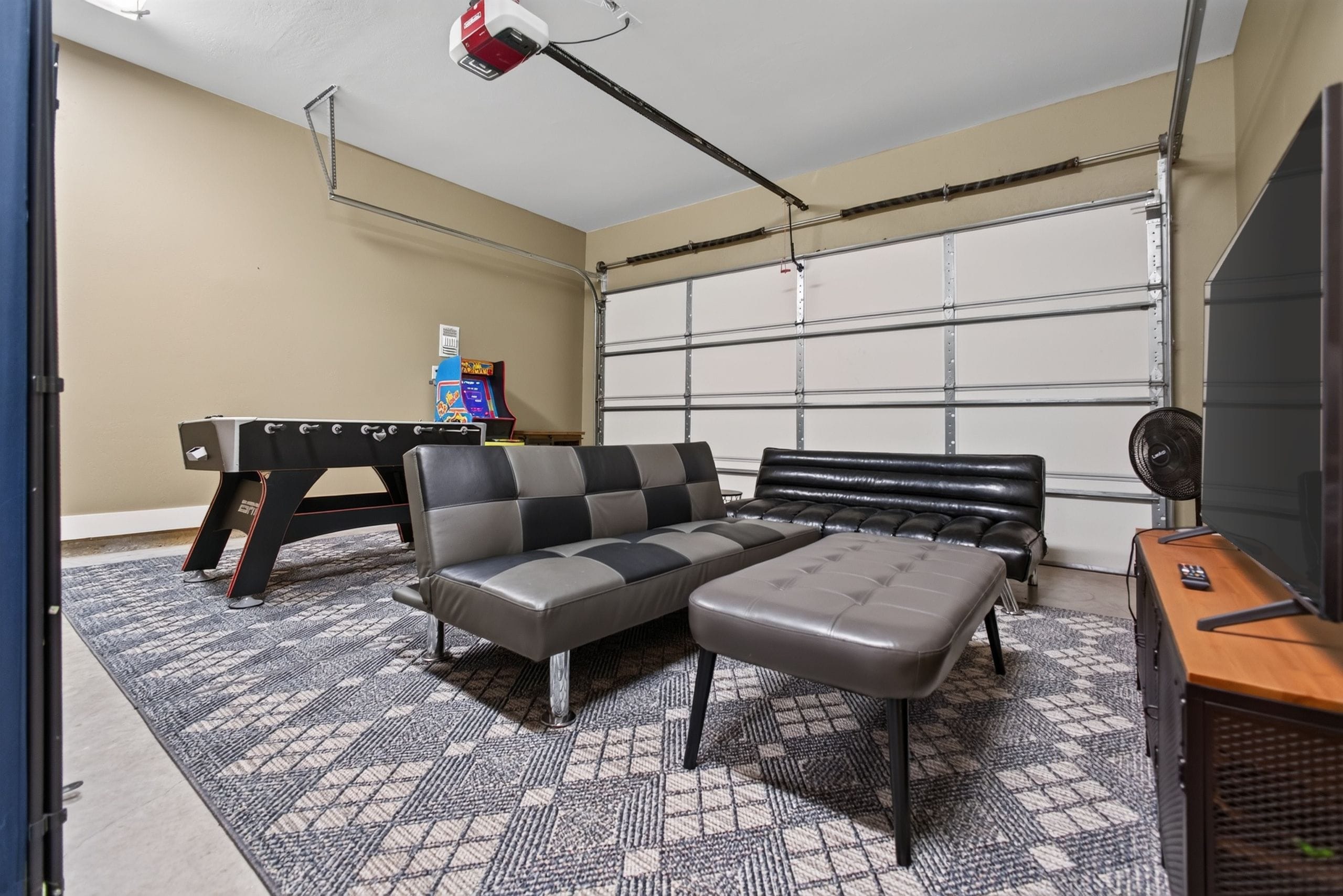 Une pièce comprenant un canapé, un pouf et une table de jeux avec une console de jeux vidéo.