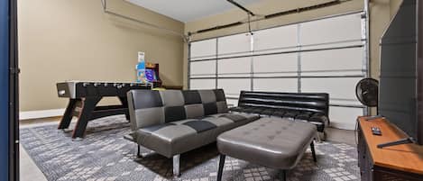 Une pièce comprenant un canapé, un pouf et une table de jeux avec une console de jeux vidéo.