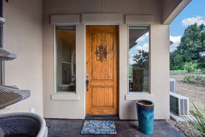 Una puerta de madera con un tirador metálico decorativo, un felpudo y un ventanal grande a la derecha.