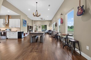 Una cocina amplia con una isla central, un comedor con barra y ventanas grandes con vistas al exterior.