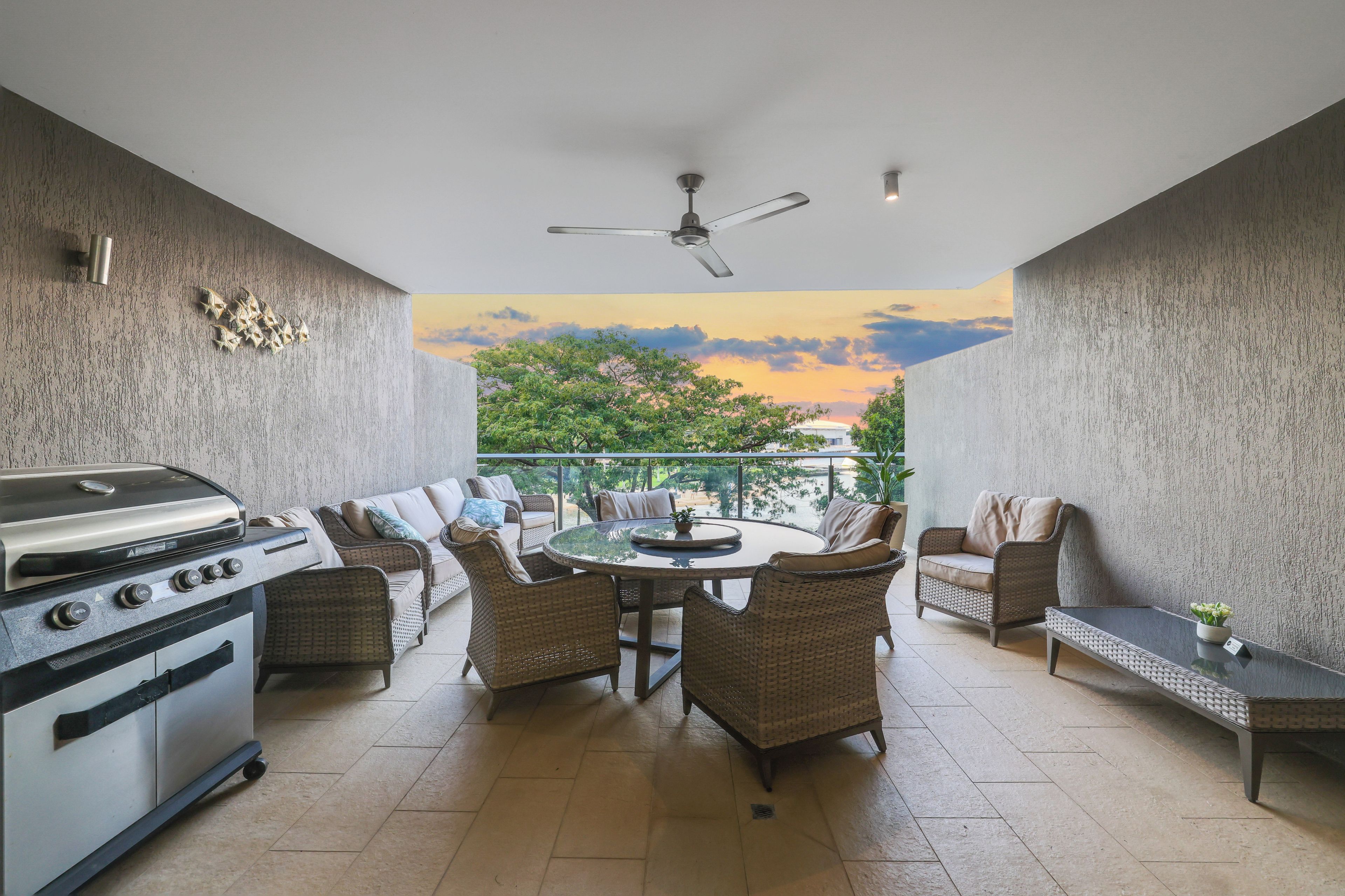 A balcony with a grill, wicker furniture, and a view of trees and sky.