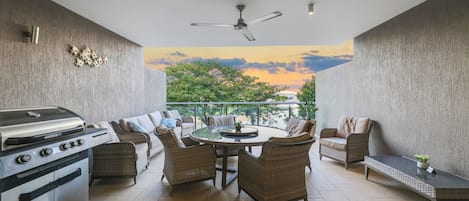 A balcony with a grill, wicker furniture, and a view of trees and sky.