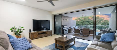 A modern living room with a flat-screen TV, a ceiling fan, and a view of an outdoor patio with furniture.