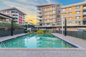 A swimming pool surrounded by modern buildings with balconies and a clear sky. - Lagoon Glow Waterfront Sunsets and Poolside Days (Darwin)