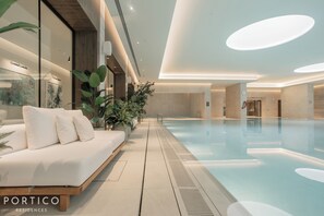 Ein moderner Innenbereich mit Schwimmbad, einer weißen Couch und Topfpflanzen.