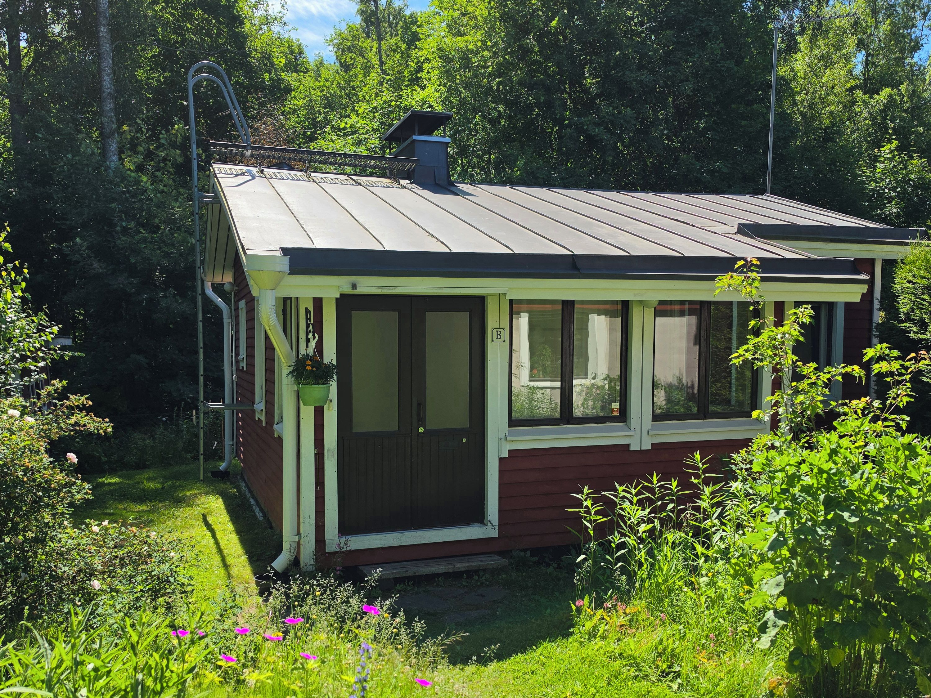Et lille, et-plans hus med skrå tag, en veranda med gelænder og en skorsten.