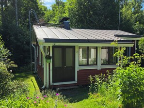 Et lille, et-plans hus med skrå tag, en veranda med gelænder og en skorsten.