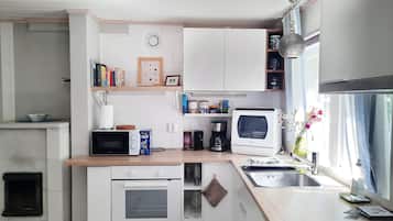 A compact kitchen with white cabinets, a microwave, a coffee maker, and a sink.